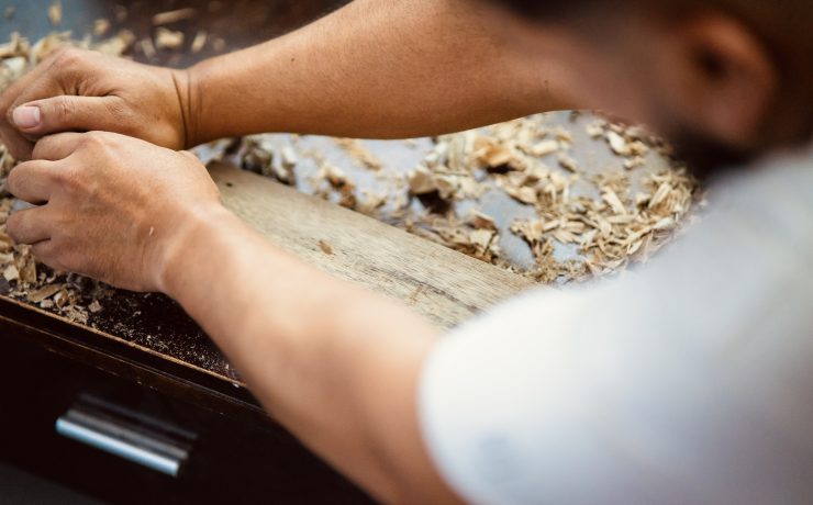 Wood shavings carpenter working with a metal spokeshave and a blurry background. Light beige colored poplar wood with slight curves in it. Vintage woodworking, handwork, handmade